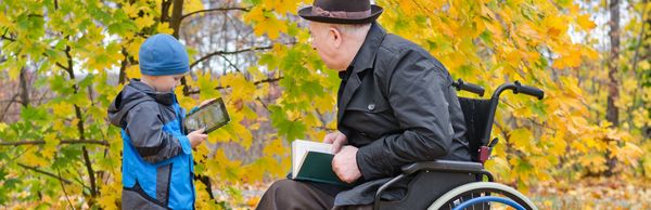Junge mit Tablet und älterer Mann im Rollstuhl mit Buch 