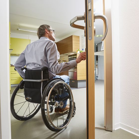 Mann im Rollstuhl öffnet barrierefreie Tür