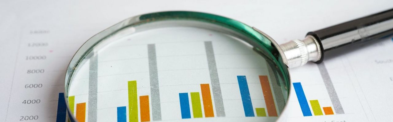 Lupe liegt auf Unterlagen mit Statistiken und Zahlen